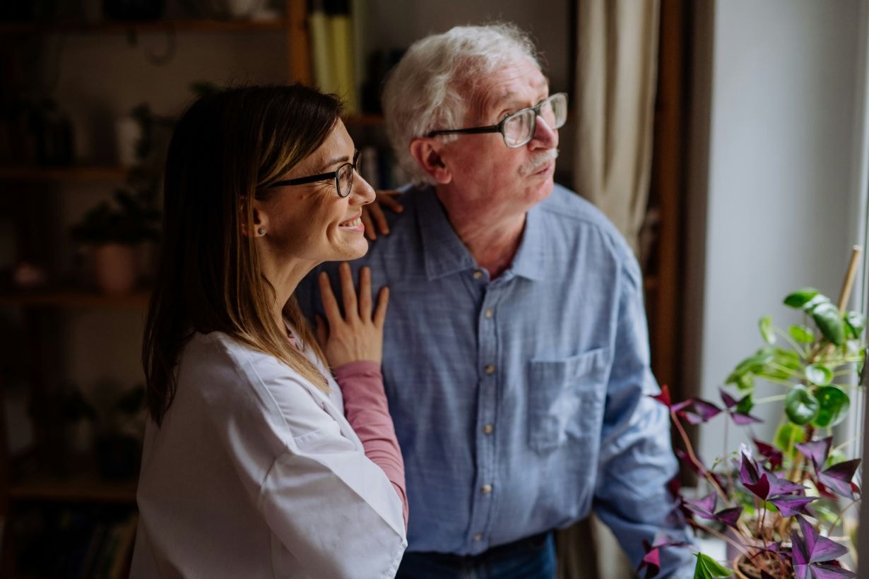 Caregiver and senior disabled man looking out