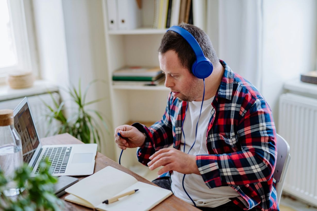 Man with Down syndrome sitting at his desk with this laptop and listening to music