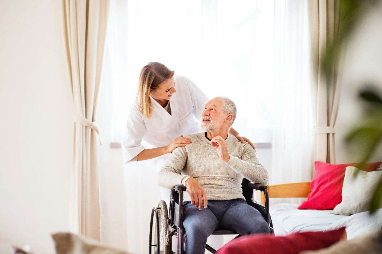 Lady caregiver comforting old man in his wheelchair