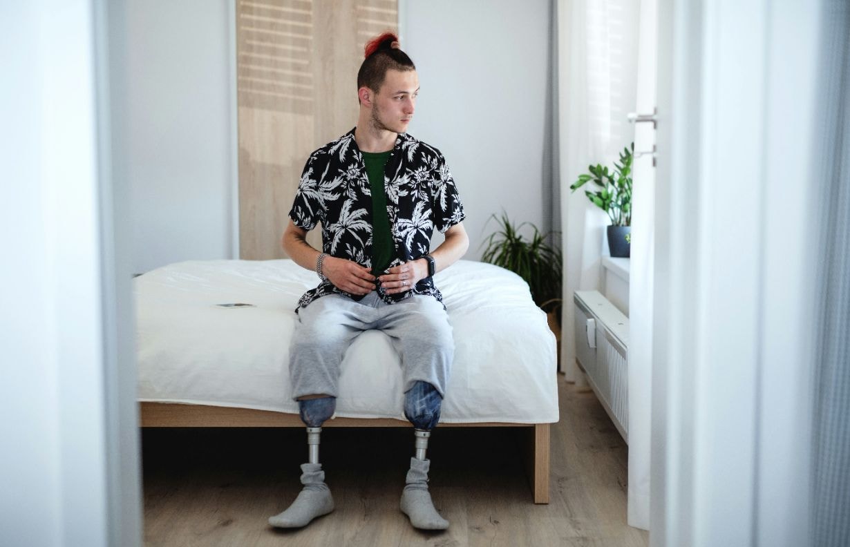 Disabled young man sitting on the bed with leg prothetics