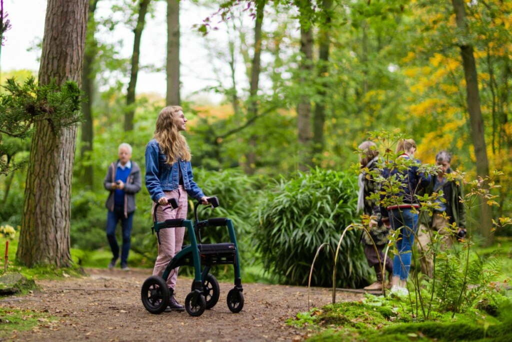 A young woman with a walking aid, supported by the National Disability Insurance Scheme, and a group of people enjoy a stroll in a lush, green park.