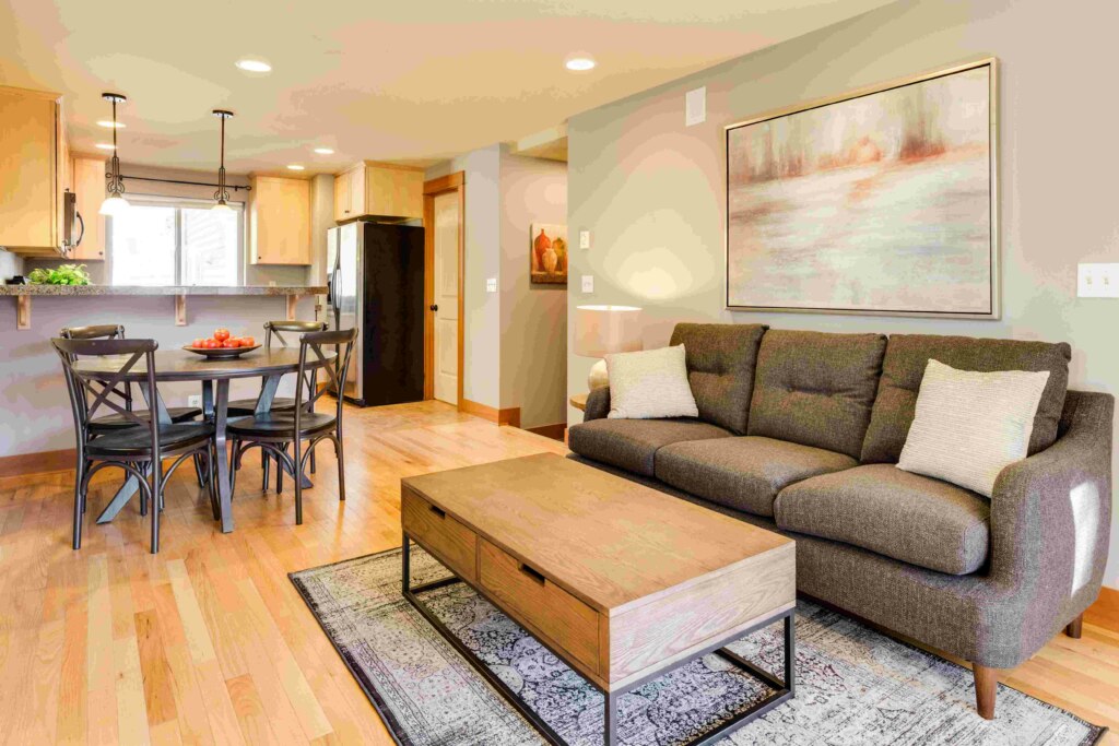 A well-lit, modern living room with an adjoining dining area, featuring a brown sofa, wooden coffee table, and a large wall painting suitable for NDIS Housing.