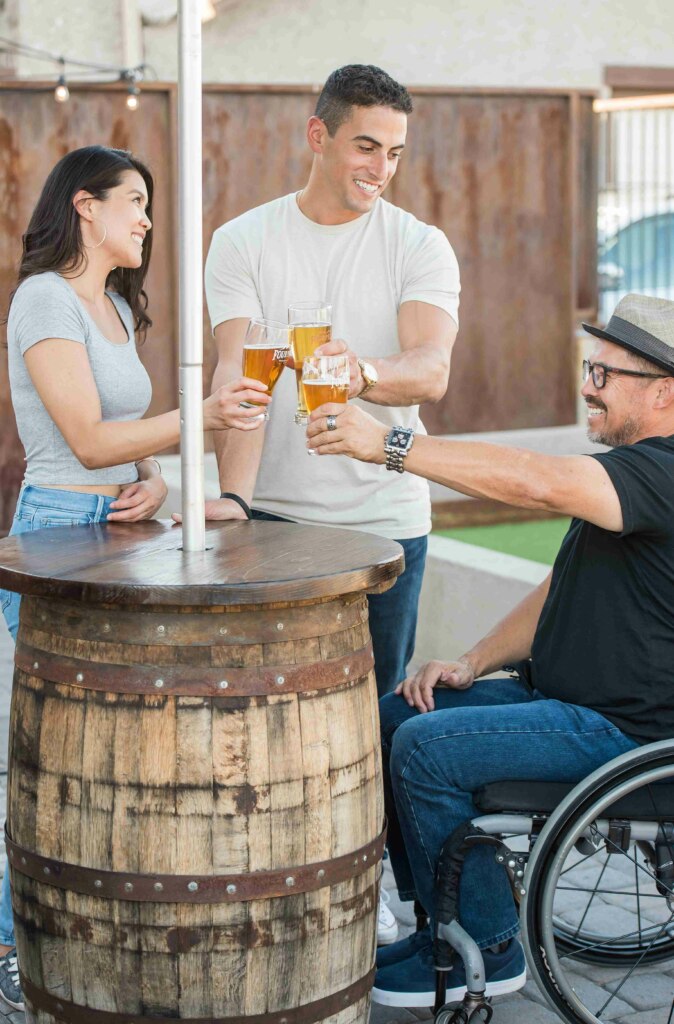 Three friends enjoying drinks and a conversation, one of whom is using a wheelchair.