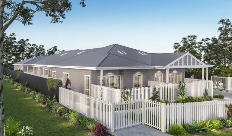 A modern, single-story building with gray siding and a pitched roof, surrounded by a white picket fence and landscaped garden, is an ideal piece of real estate in Wamberal, situated next to a pathway.