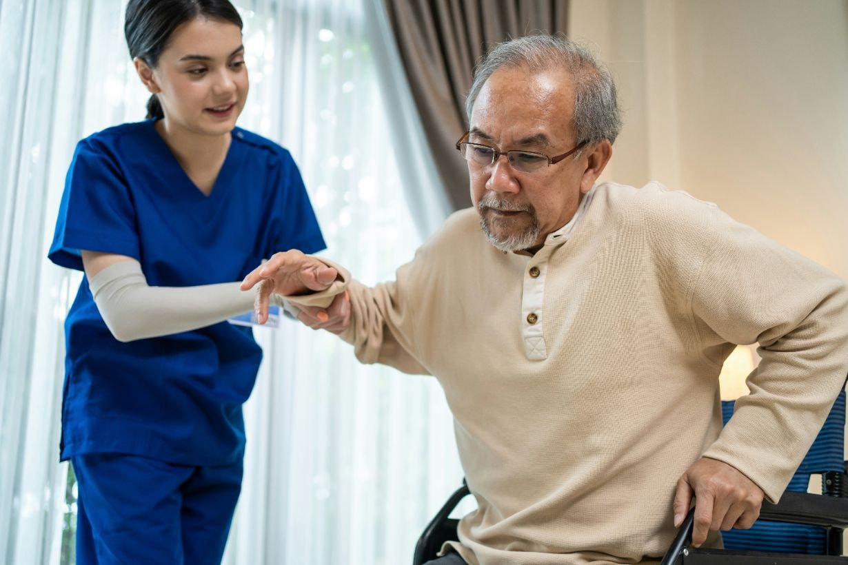 Lady caregiver helping old man to stand up from his wheelchair