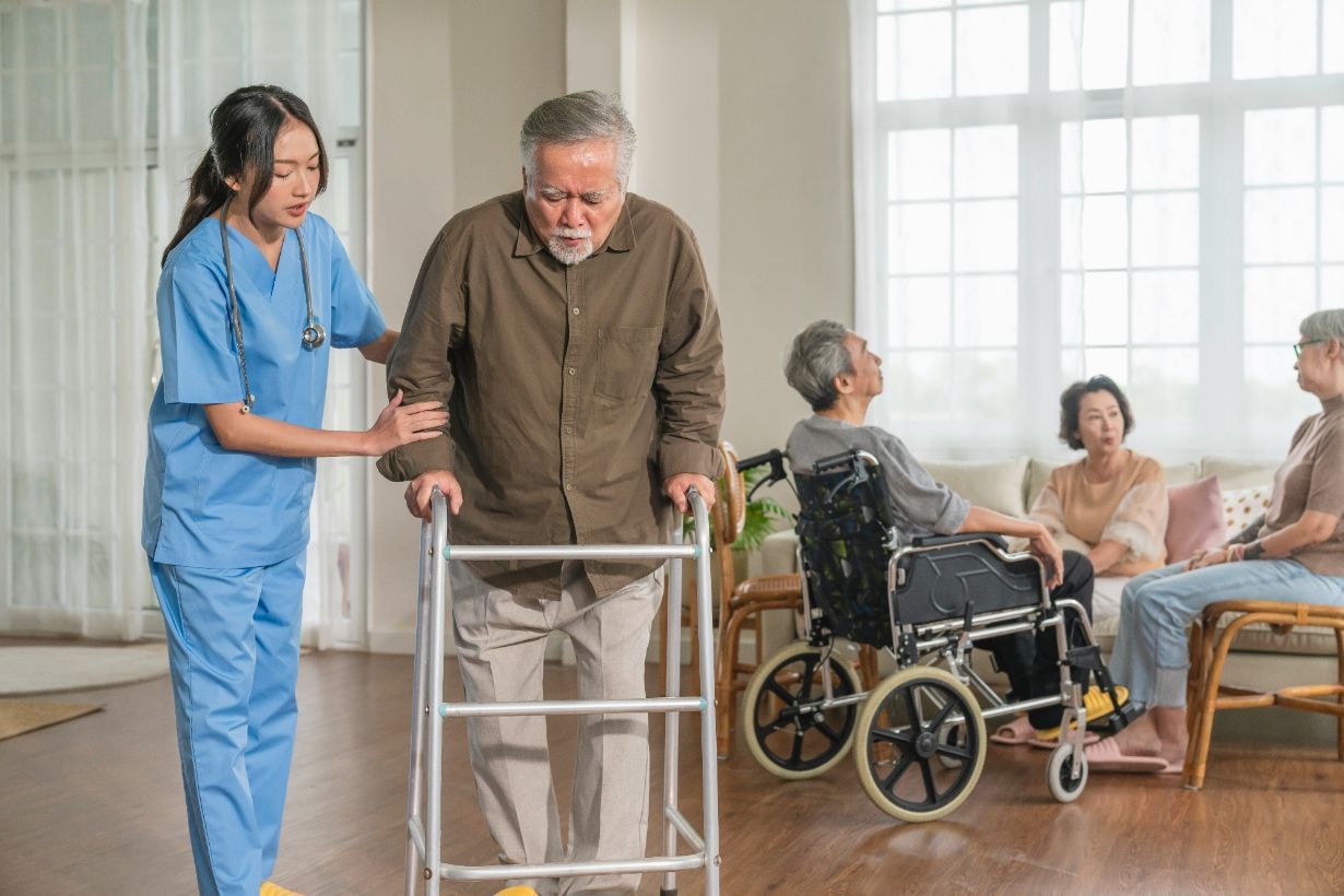 Caregiver helping senior man to use the walker to walk