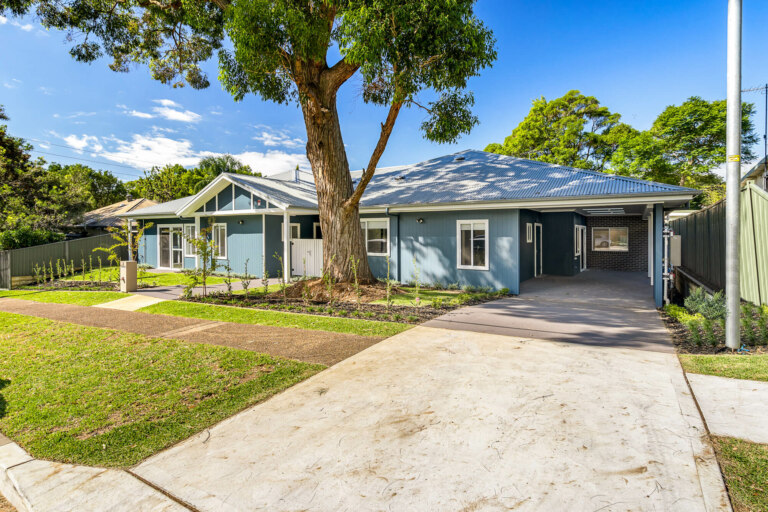 Located in the heart of Sutherland Shire, this charming single-story blue house boasts a metal roof, multiple windows, an attached carport, and a grassy yard under a large tree. Enjoy sunny Sydney days at 30A.