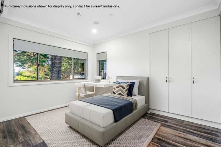 A modern bedroom in Narraweena with a single bed, blue and white bedding, a desk with a chair by the window, and built-in wardrobes. A disclaimer about furniture display is visible on the top left. Ideal for those seeking comfort in the Northern Beaches of Sydney.